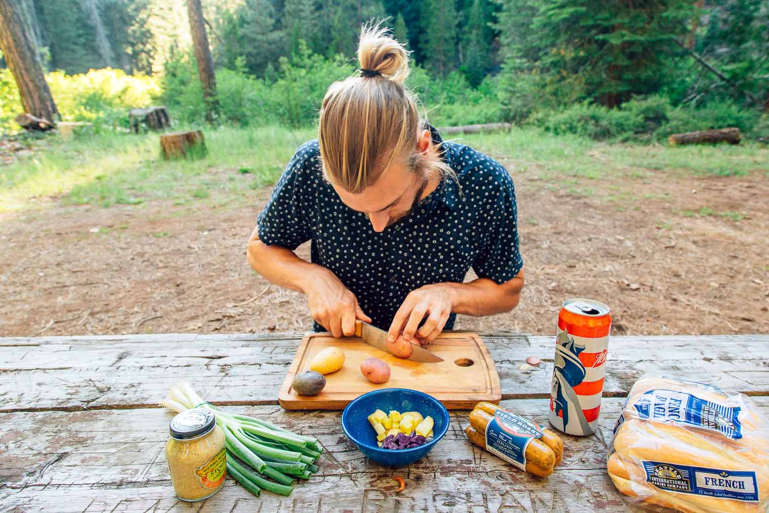 Michael is sitting at a camping table chopping potatoes