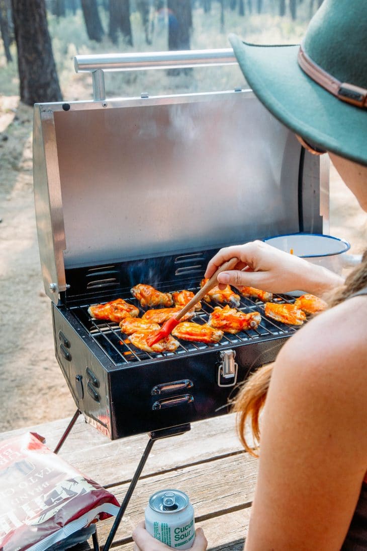 Megan basting wings on a grill with hot sauce