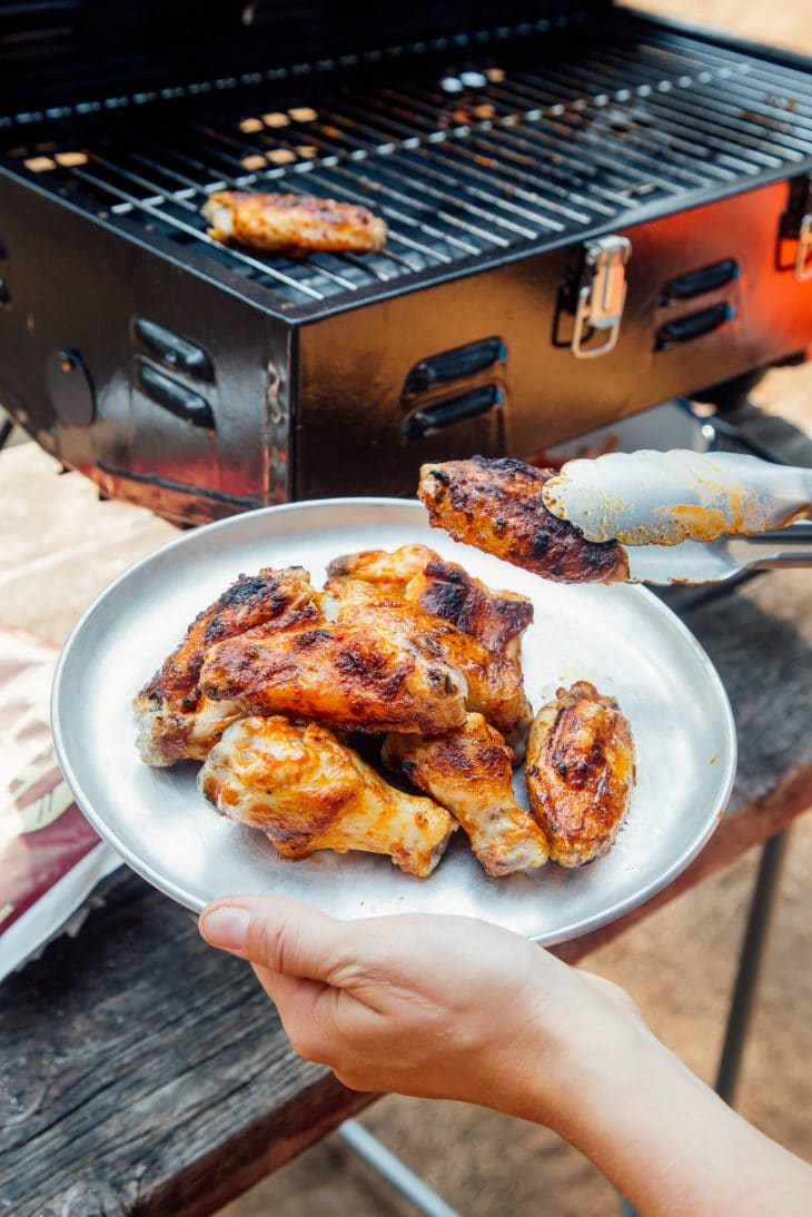 Megan using tongs to pick up a wing off of a grill and transfer to a plate she is holding