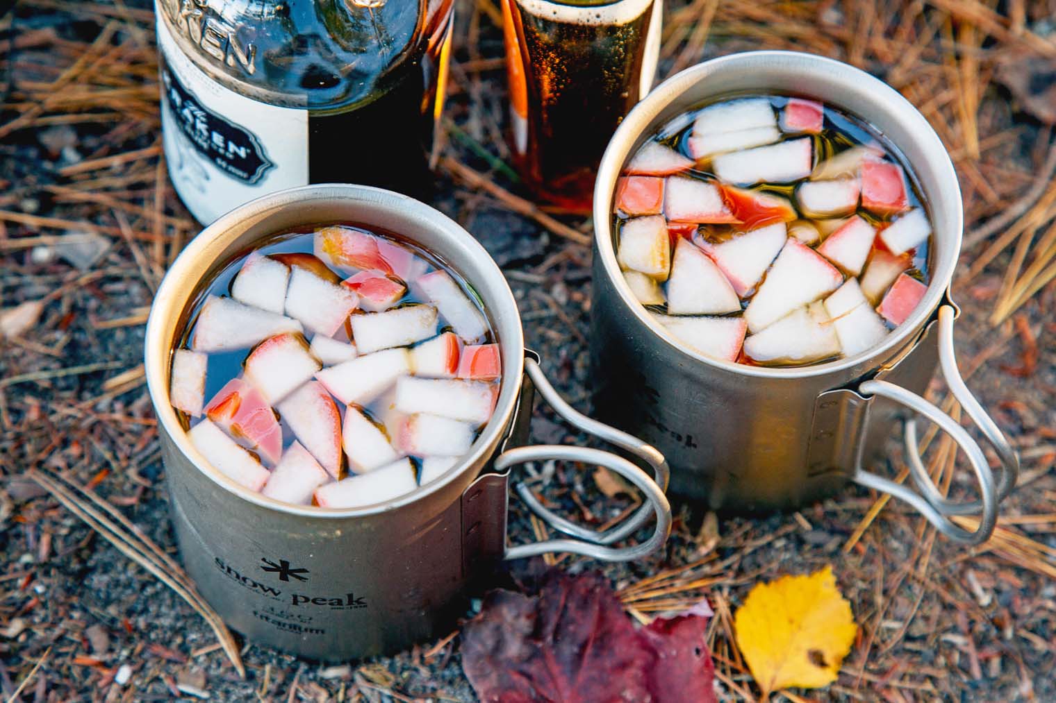 Two mugs of Apple maple cocktails on a leafy surface