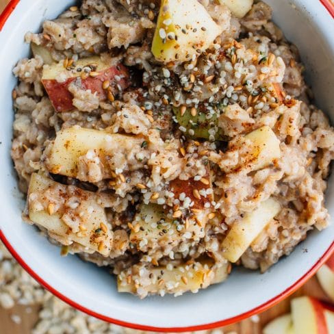 A red and white bowl filled with oatmeal topped with apples and seeds