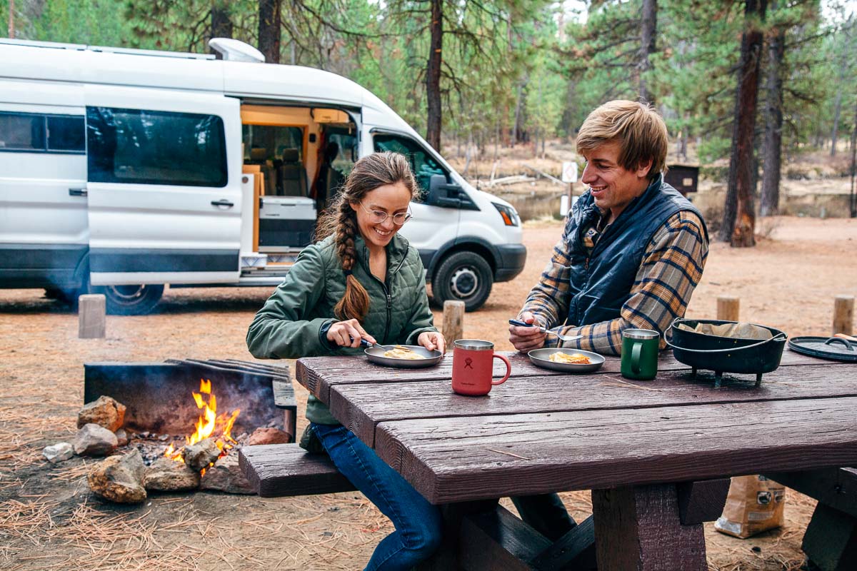 Megan and Michael sitting at a picnic table at a campsite. There is a Dutch oven on the table and they are sharing a piece of apple pie