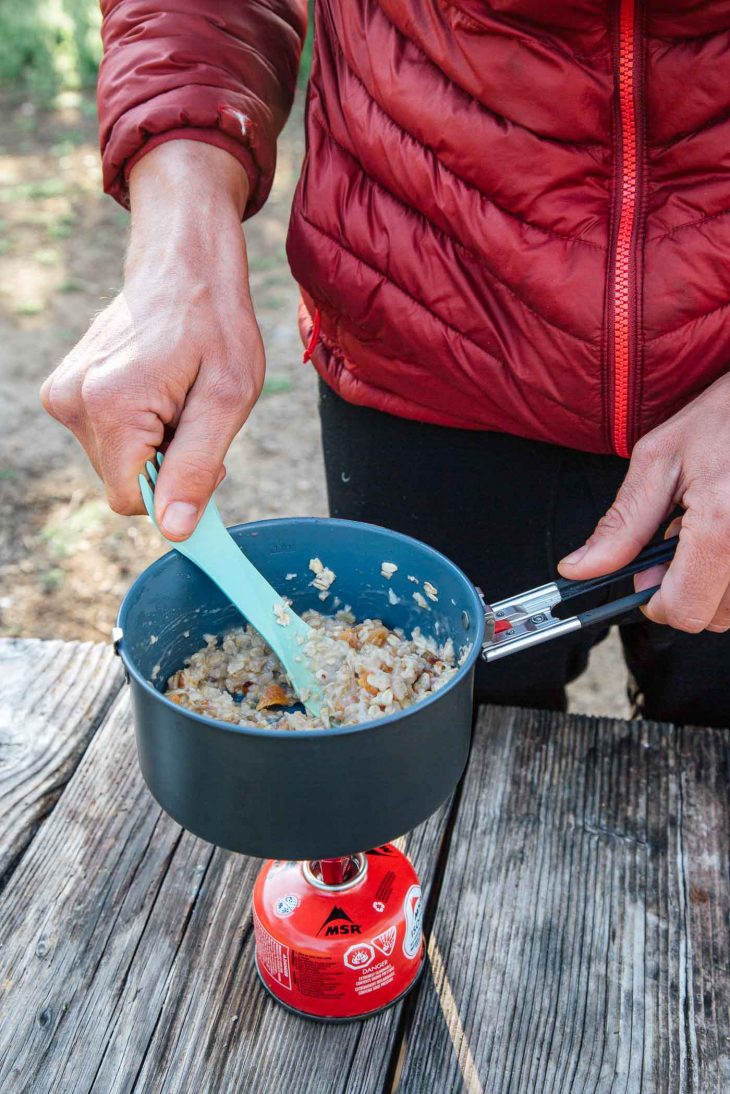 Man cooking in a pot over a small backpacking stove.