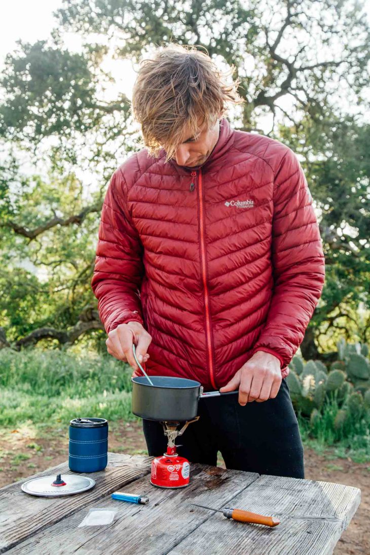 Michael standing at a camp table stirring a pot on a backpacking stove.