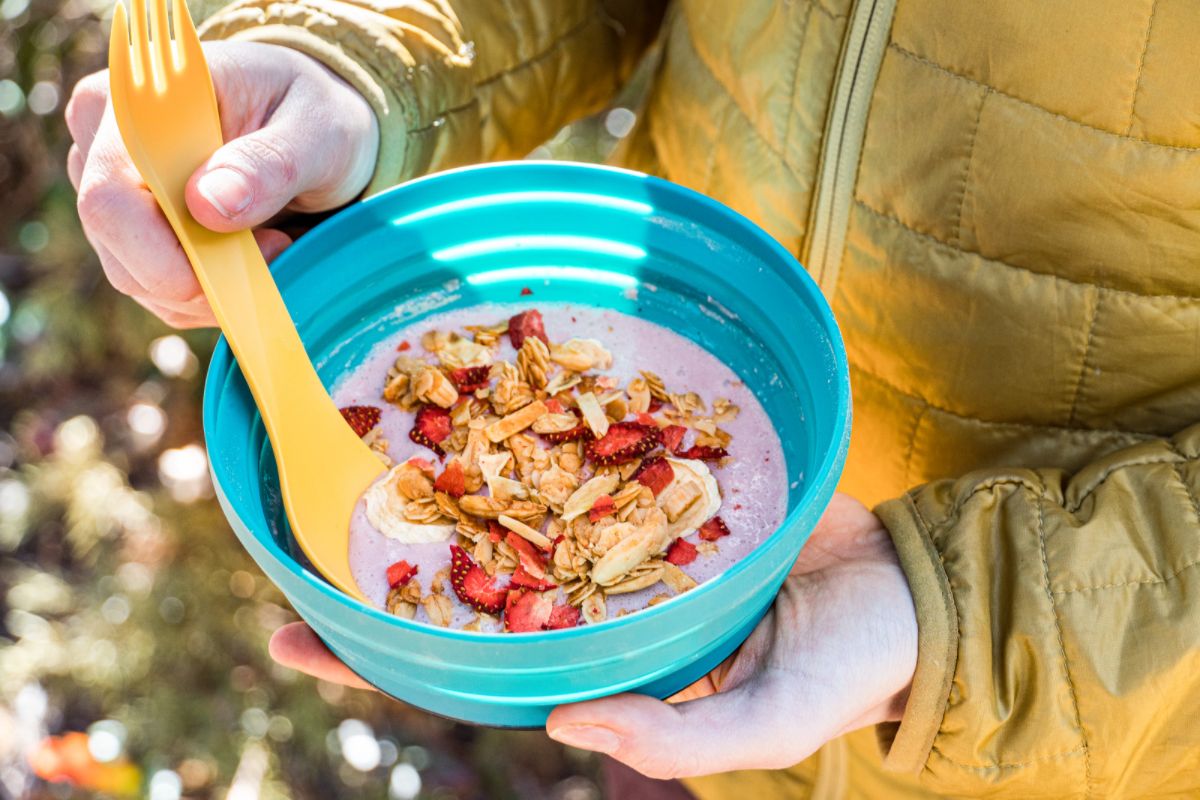 Megan holding a blue bowl with yogurt, granola, and fruit, and a yellow spoon