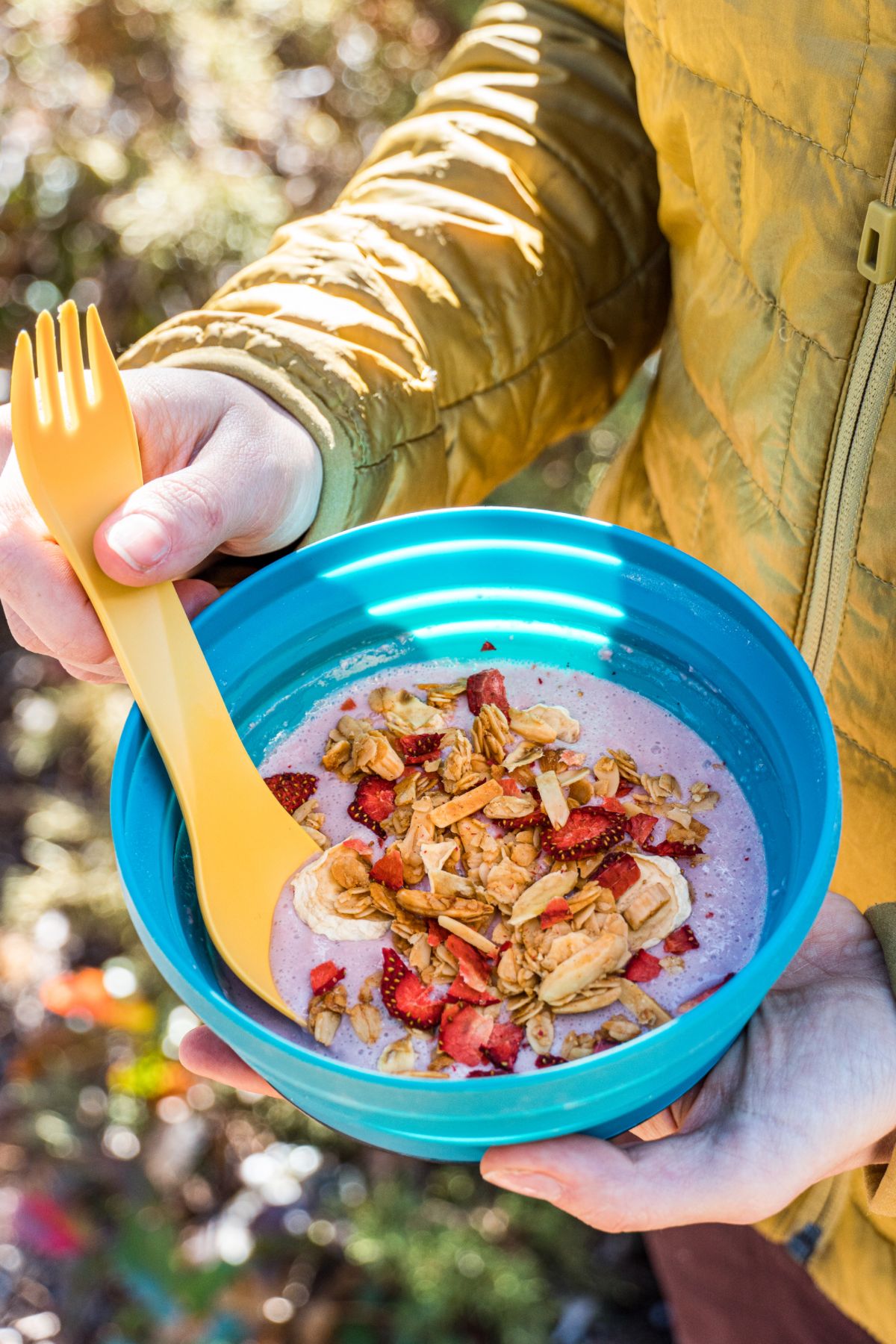 Megan holding a blue bowl with yogurt, granola, and fruit, and a yellow spoon