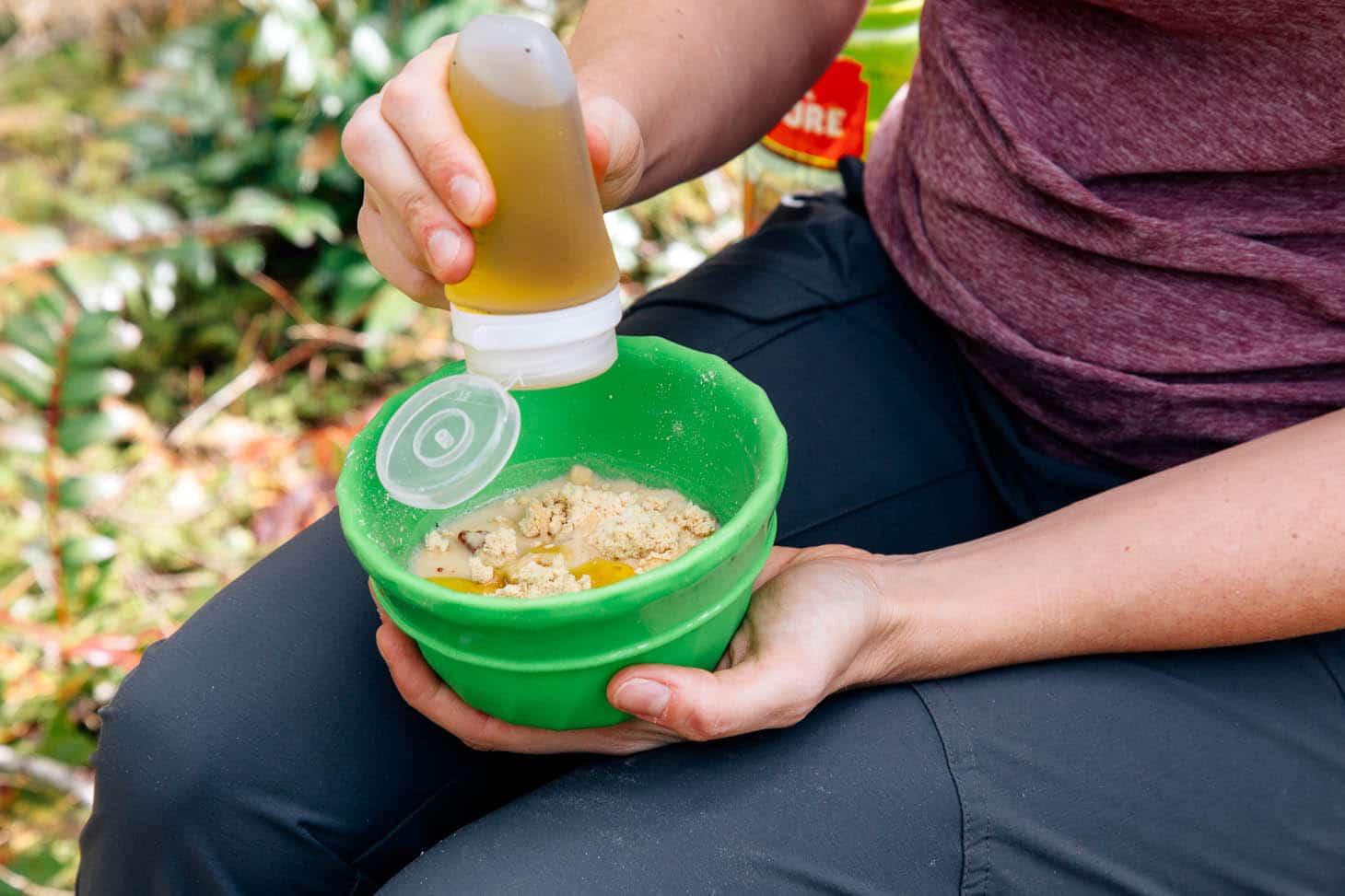 Woman adding olive oil into a bowl of hummus.