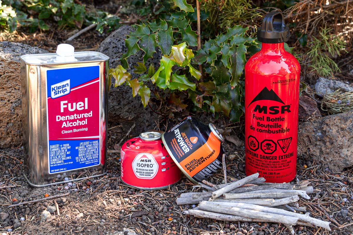 Backpacking fuel bottles: Denatured alcohol, isobutane canisters, and a red liquid fuel bottle
