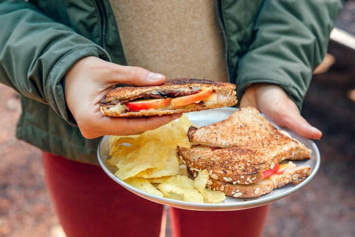 Megan holding a plate with grilled cheese and chips. She is holding one of the sandwiches.