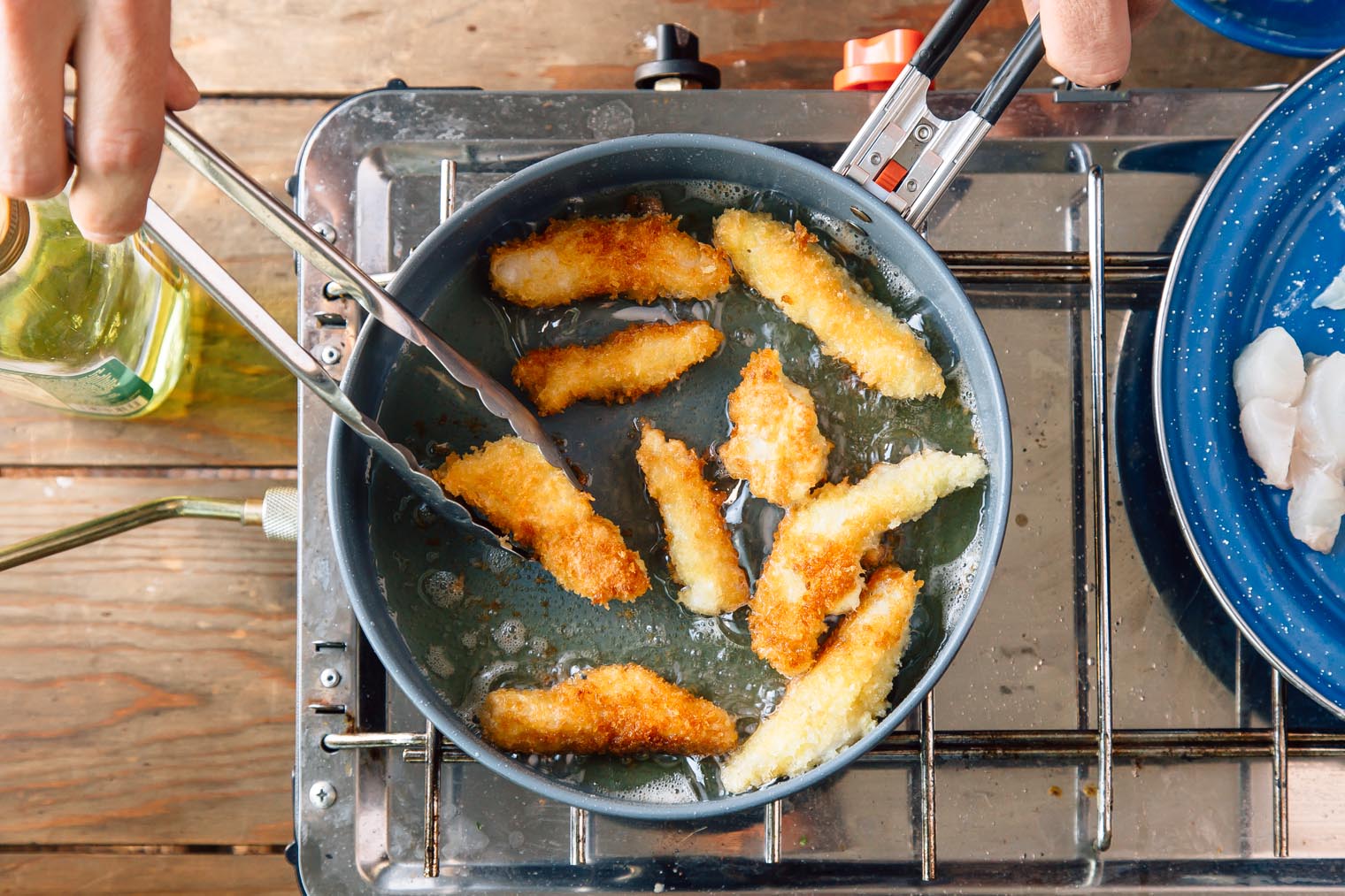 Michael frying pieces of fish in a skillet on a camping stove