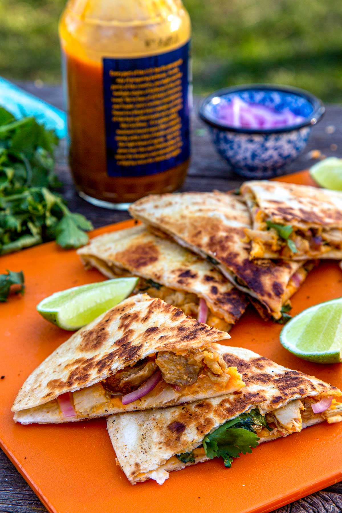 Sliced quesadillas stacked on an orange cutting board with slices of lime.