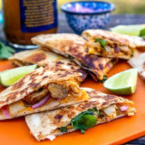 Sliced quesadillas stacked on an orange cutting board.