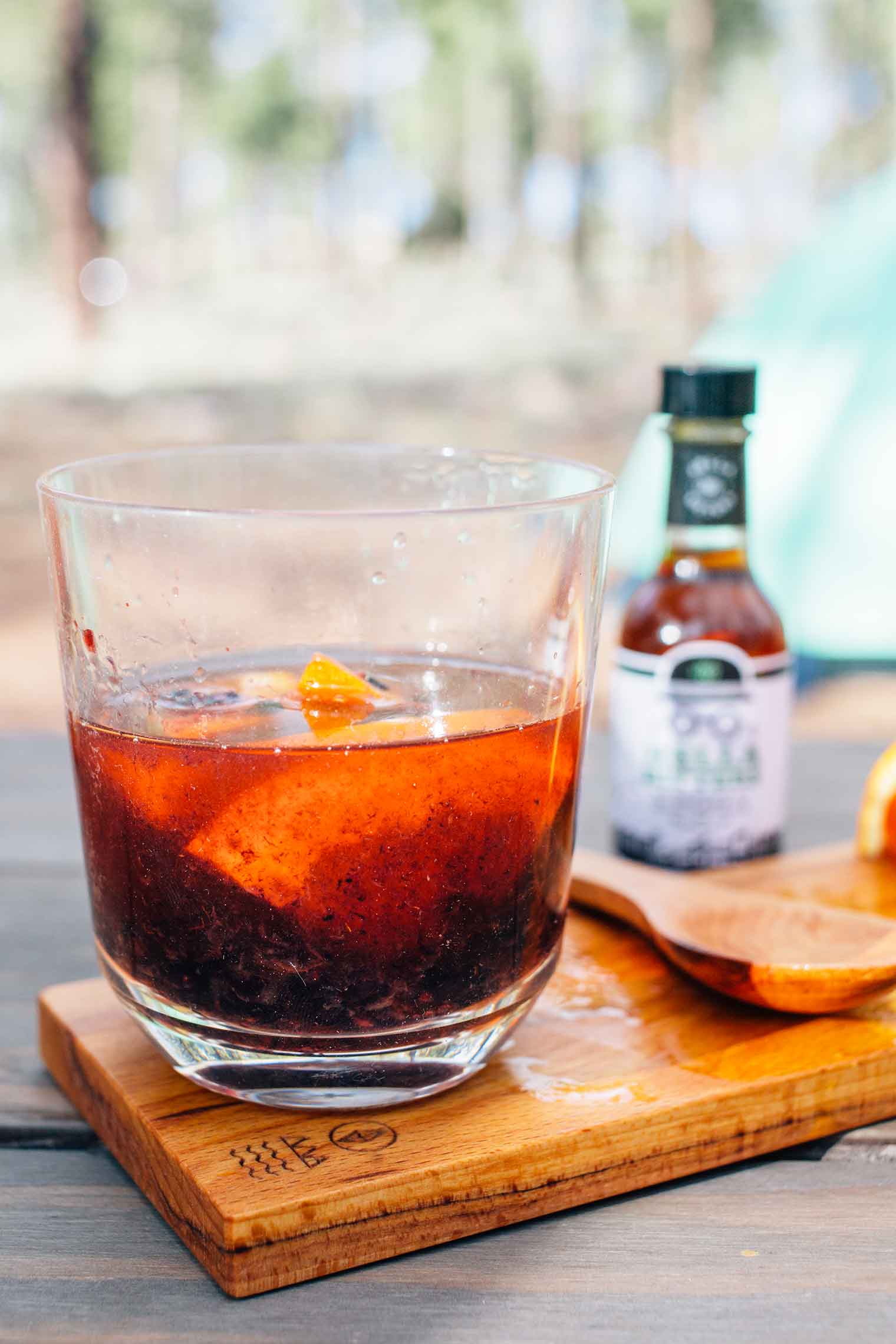 Blackberry old-fashioned in a glass next to a small bottle of bitters