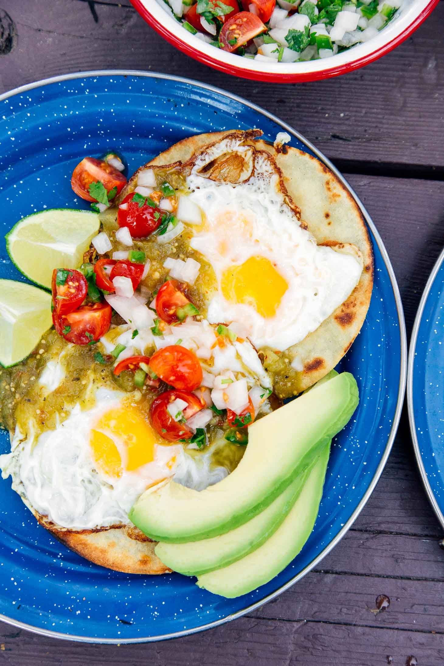 Two tortillas topped with eggs, salsa, and sliced avocado