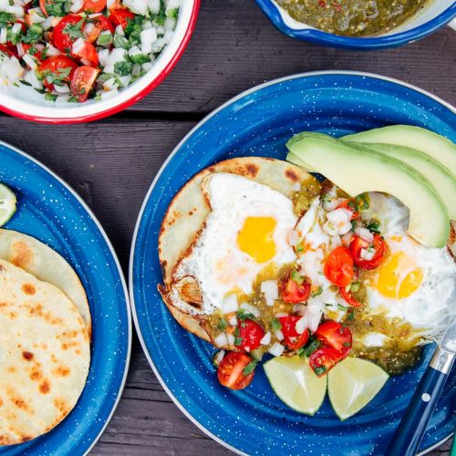 Eggs, salsa, and avocado on top of tortillas on blue camping plates.