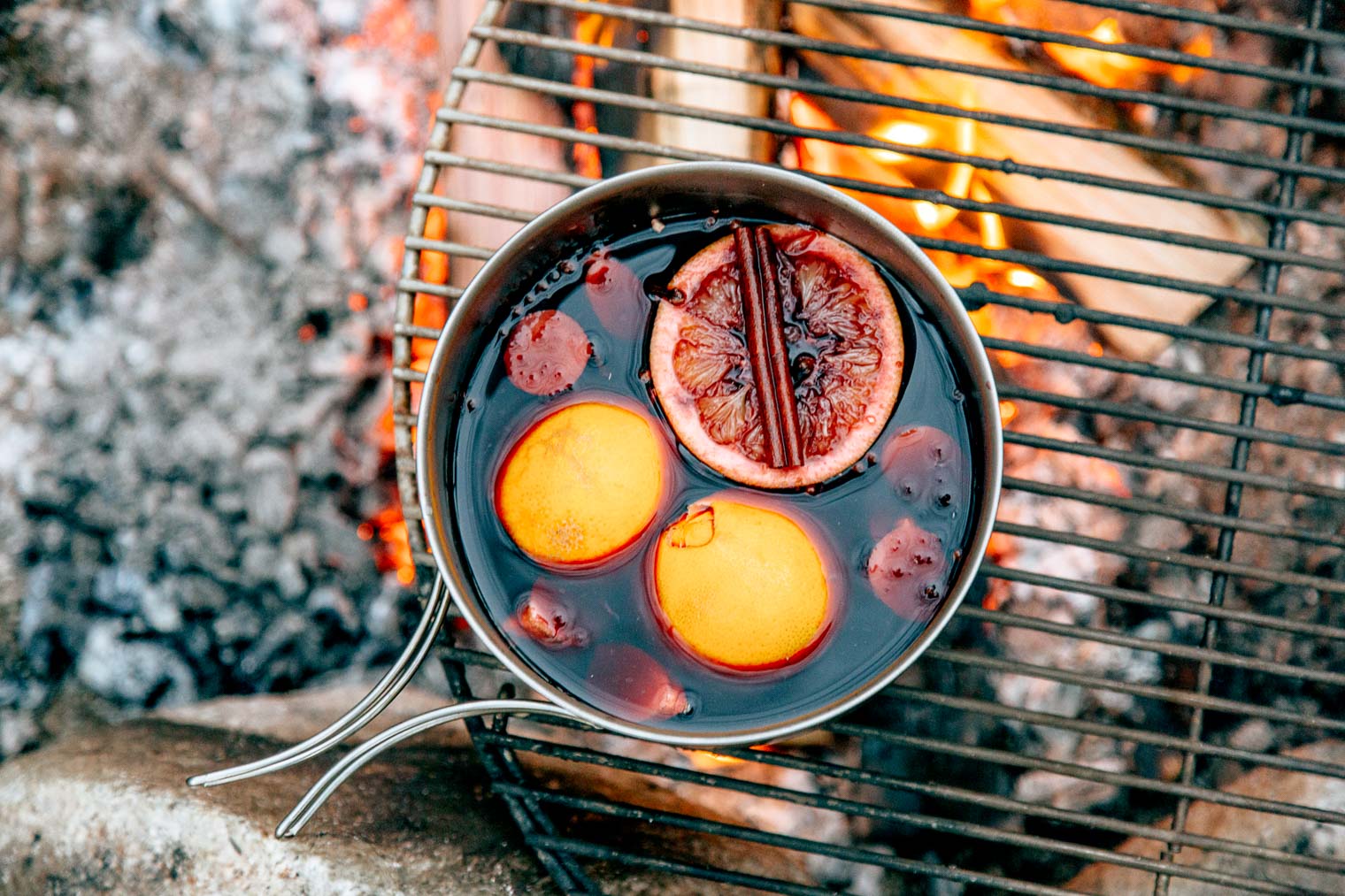 A pot of mold wine with oranges and cinnamon sticks sitting on a campfire