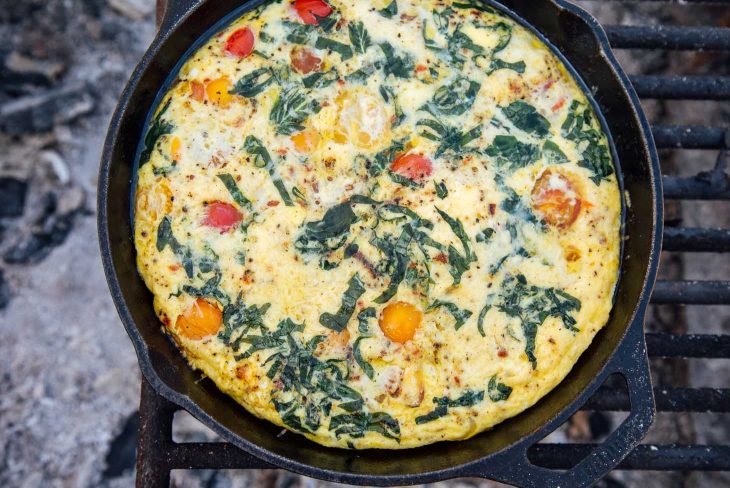 Vegetable frittata in a cast iron skillet over a campfire.