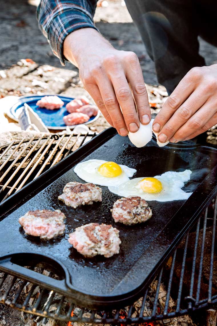 Michael cracking an egg onto a cast iron griddle on a campfire