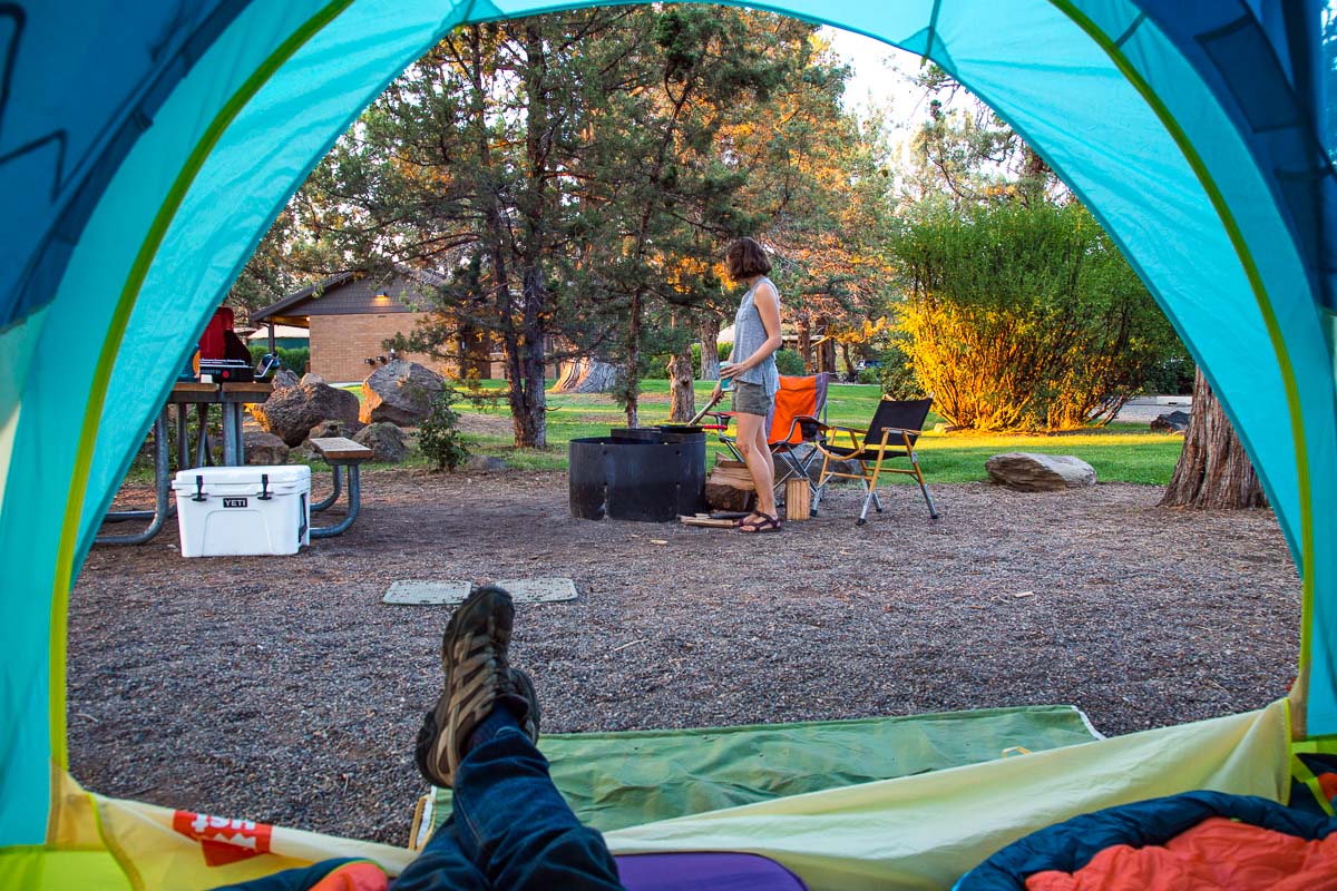 Michael's point of view looking out of a camping tent at a camp scene and Megan tending a campfire