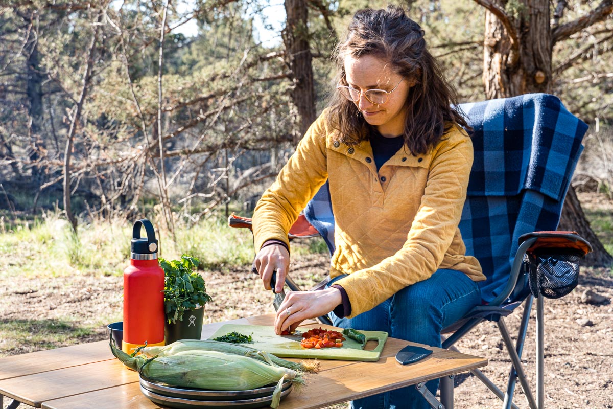 Megan is sitting in a camp chair at a small table where she is cutting vegetables