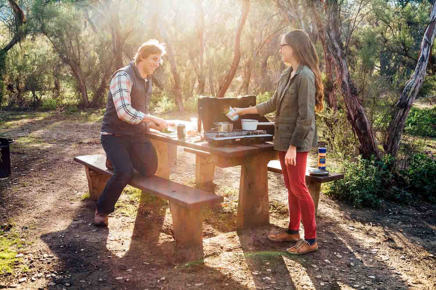 Man and woman at a campsite cooking a meal on a camping stove.