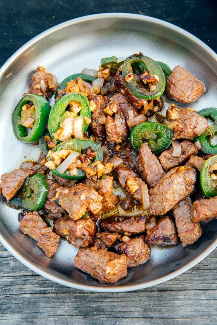 Cooked steak and jalapeños on a silver plate.