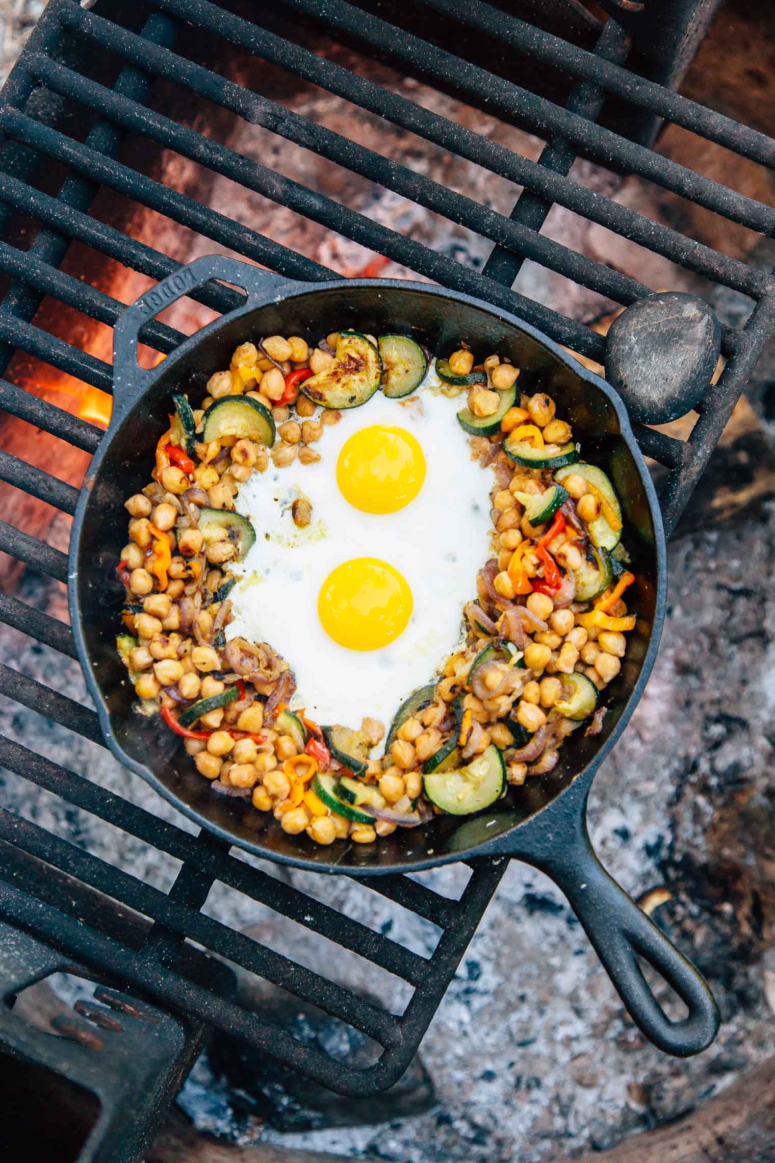 Chickpea breakfast hash with eggs in a cast iron skillet on a campfire.