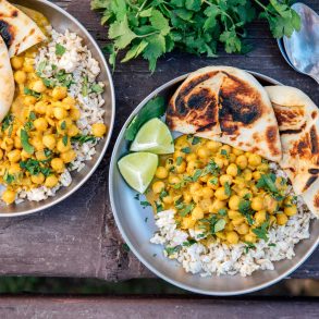 Two plates of coconut chickpea curry over rice on a camping table.