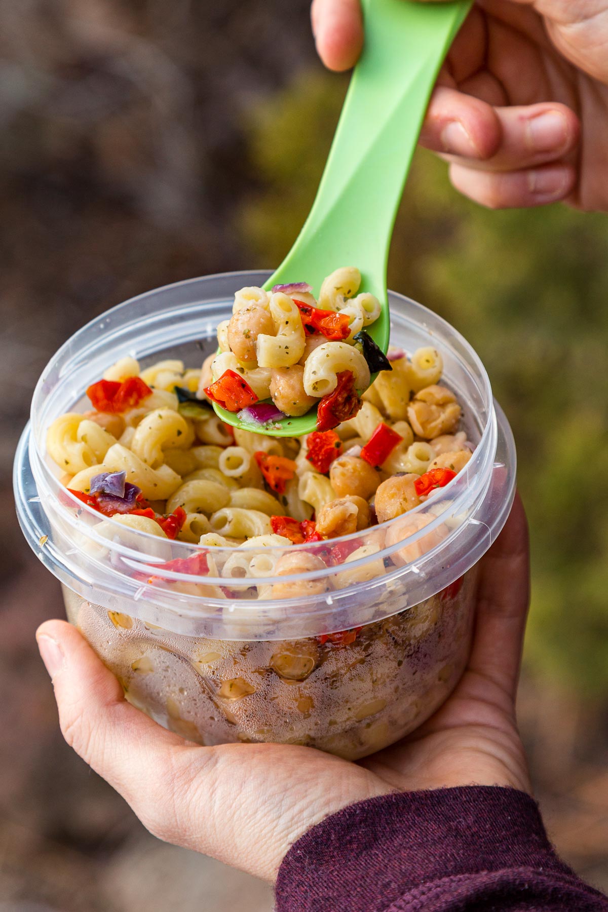 Megan holding a plastic container full of pasta salad. She's picking up a spoonful.