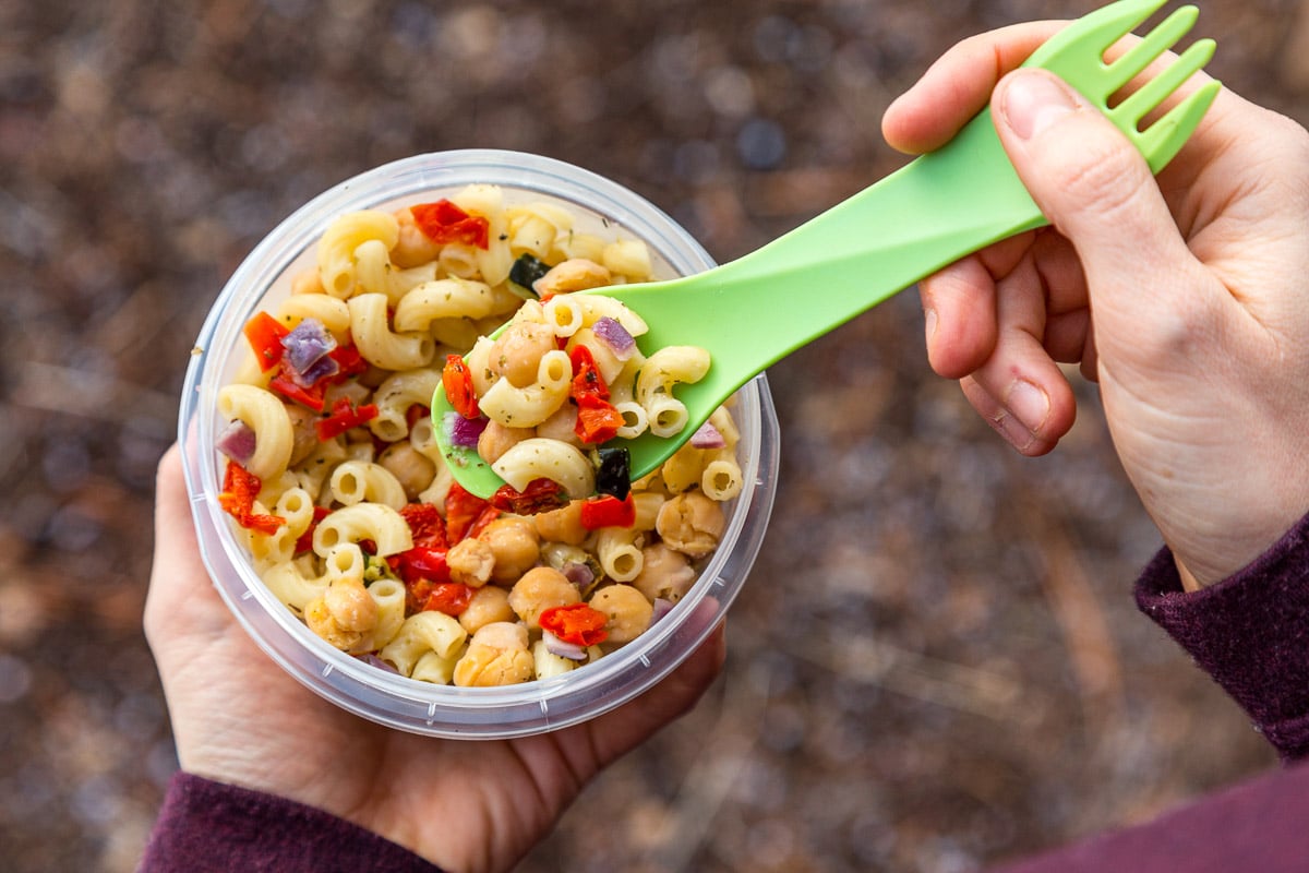 Megan holding a plastic container full of pasta salad. She's picking up a spoonful.