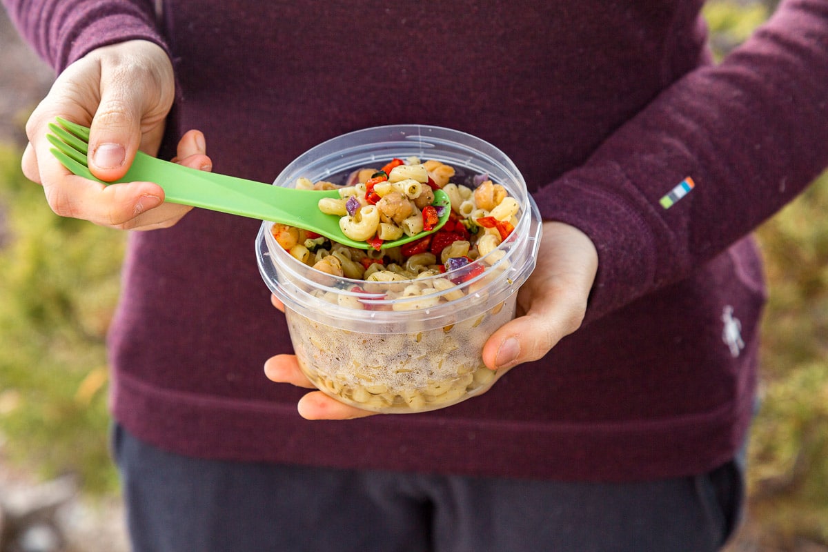 Megan holding a plastic container full of pasta salad. She's picking up a spoonful.