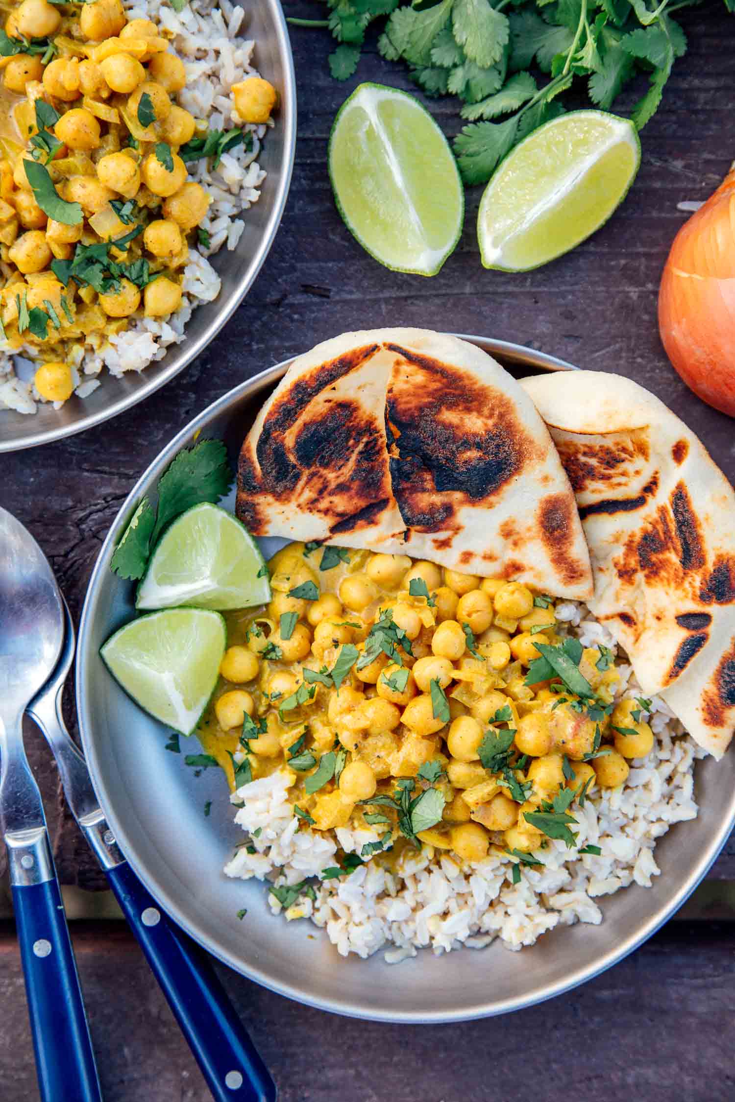 A plate of curried chickpeas over rice on a camping table with wedges of lime.