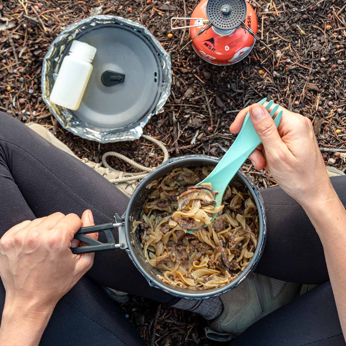 Overhead view of a person sitting cross leg and holding a pot of beef stroganoff