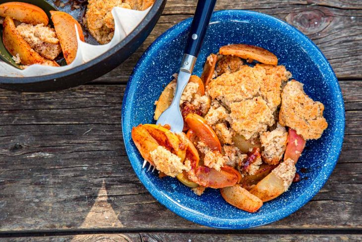 Apple cobbler in a blue bowl next to a Dutch oven