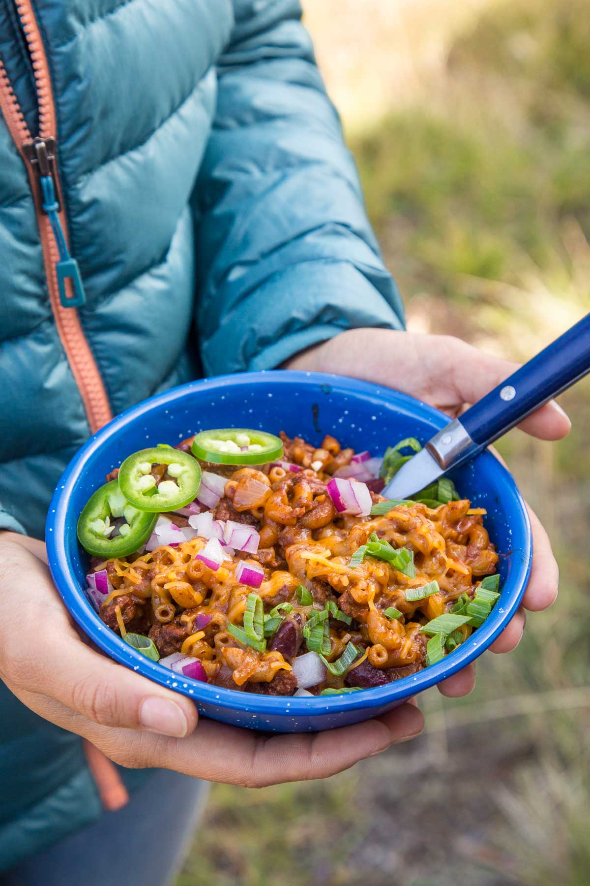 Megan holding a bowl of chili mac topped with jalapeños and cheese