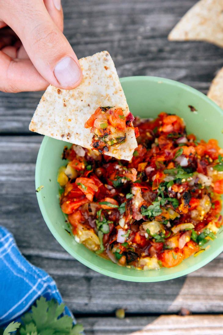 A person dipping a chip into a bowl of fire roasted salsa