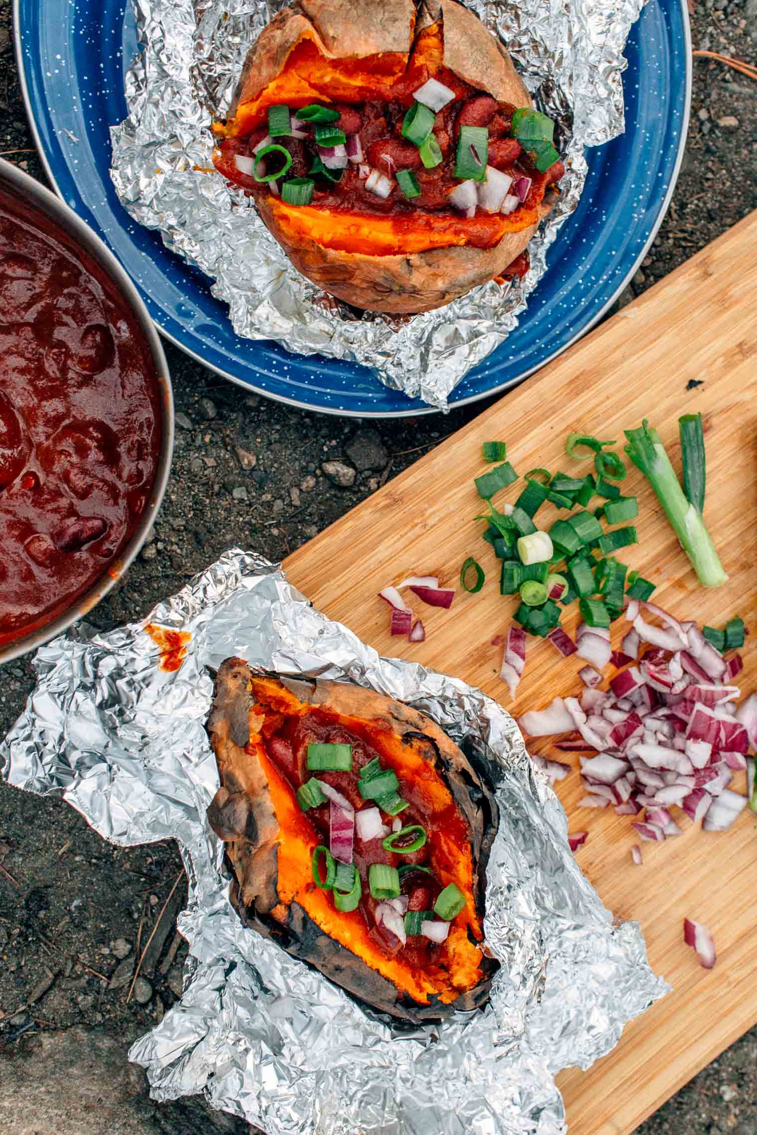 Foil wrapped sweet potatoes and chili on a blue camping plate.