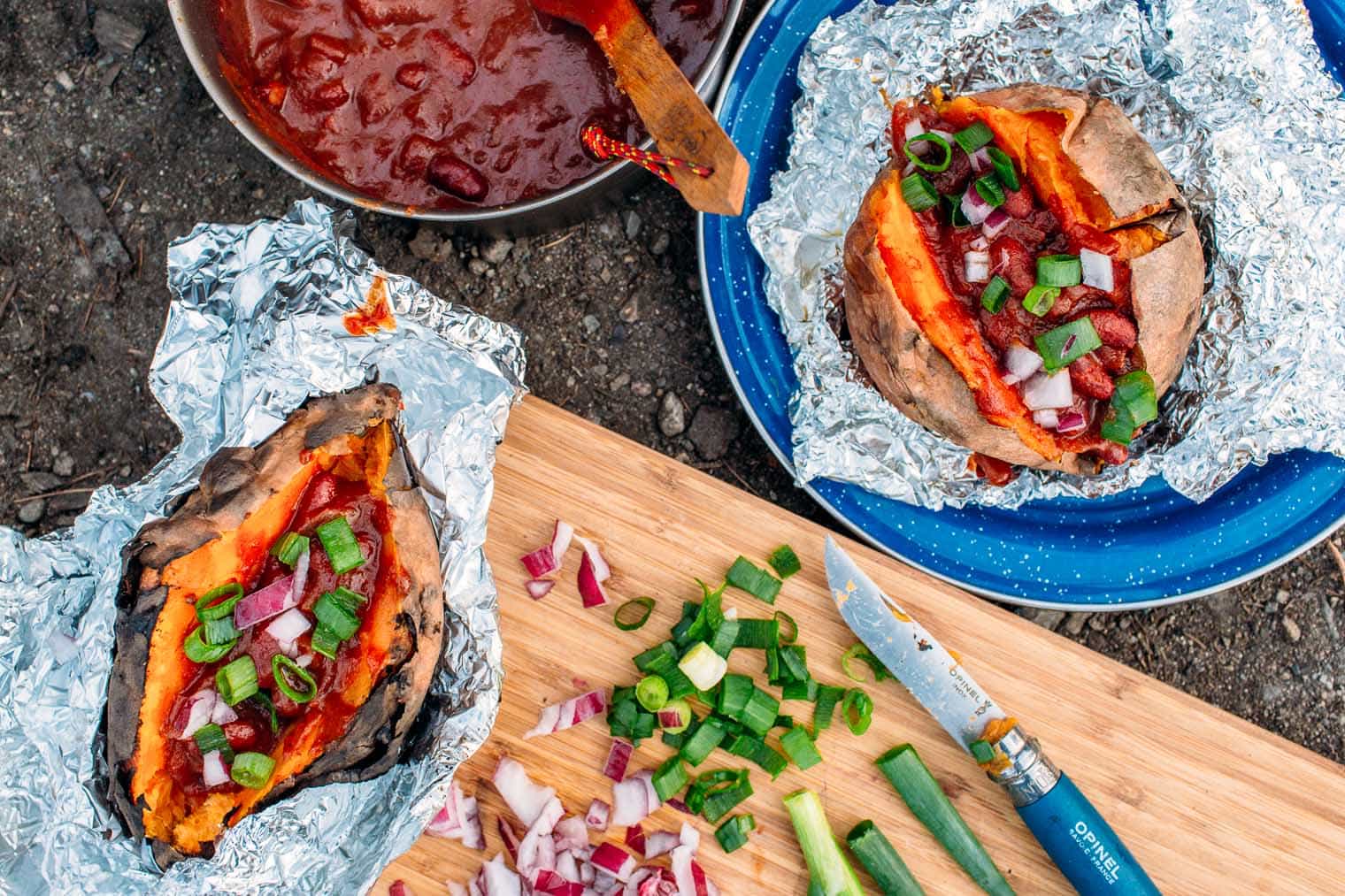 Sweet potatoes stuffed with chili in foil surrounded by toppings