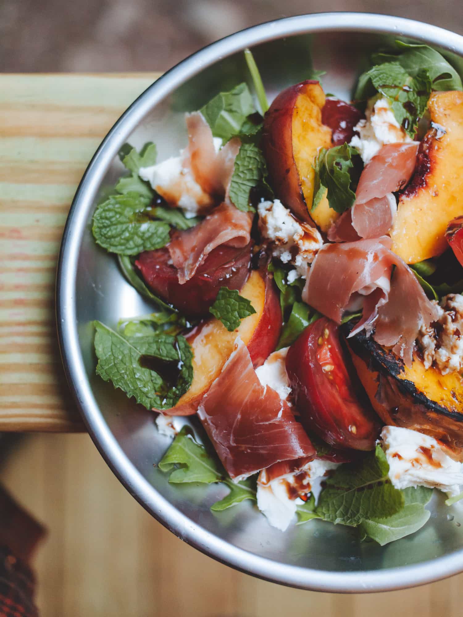 Grilled peach caprese salad on a silver camping plate.