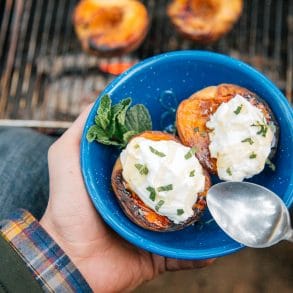 Two grilled peaches topped with yogurt in a blue bowl