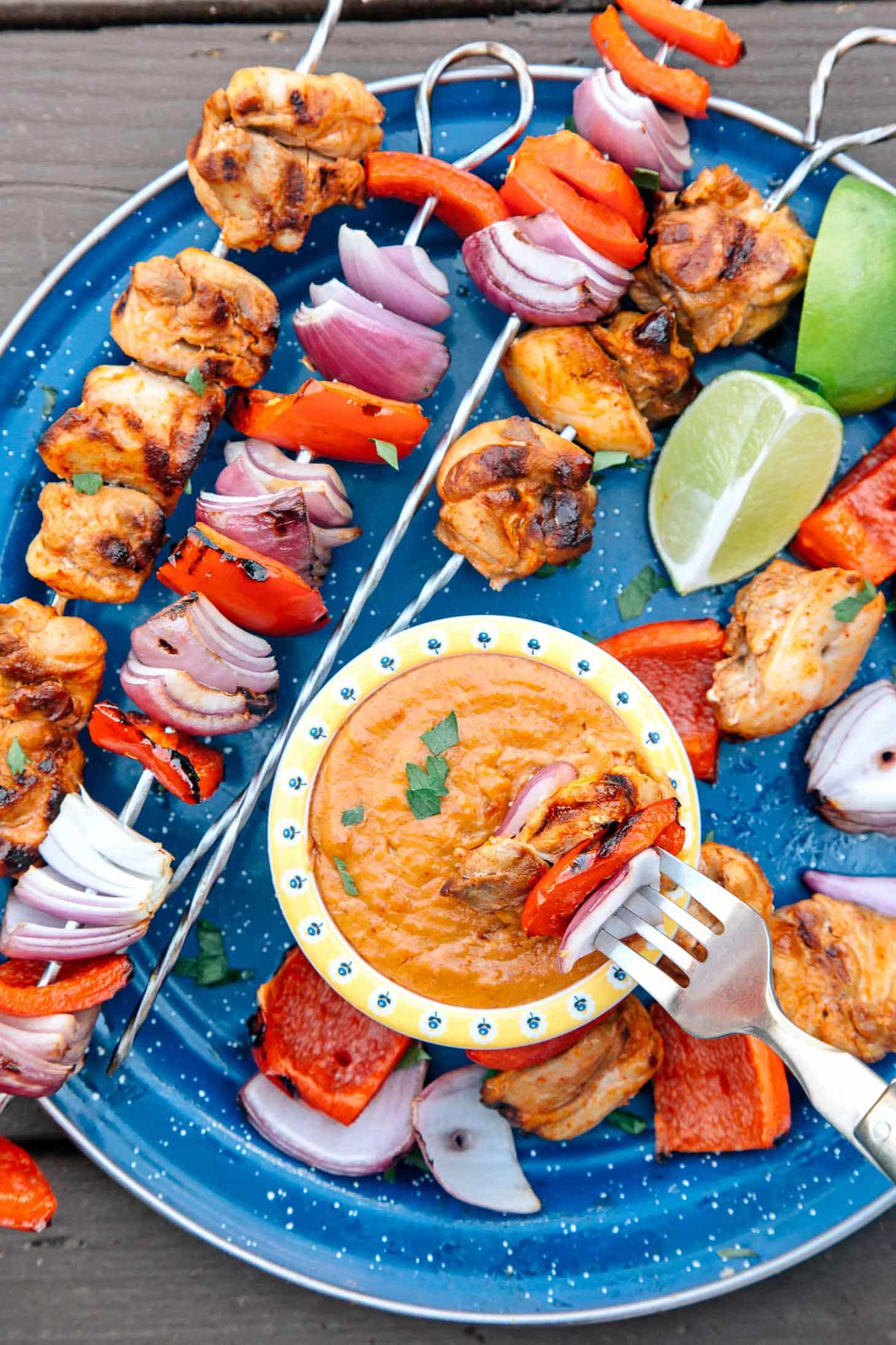 Thai grilled chicken skewers on a blue camping plate with a small bowl of peanut dipping sauce.