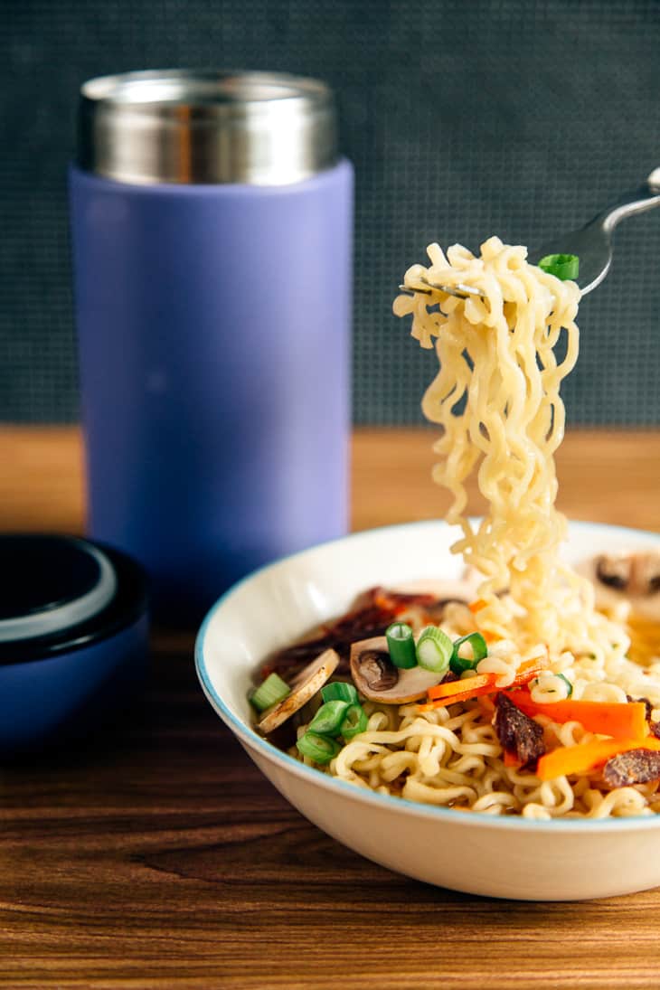 Fork picking ramen noodles up out of a bowl of soup