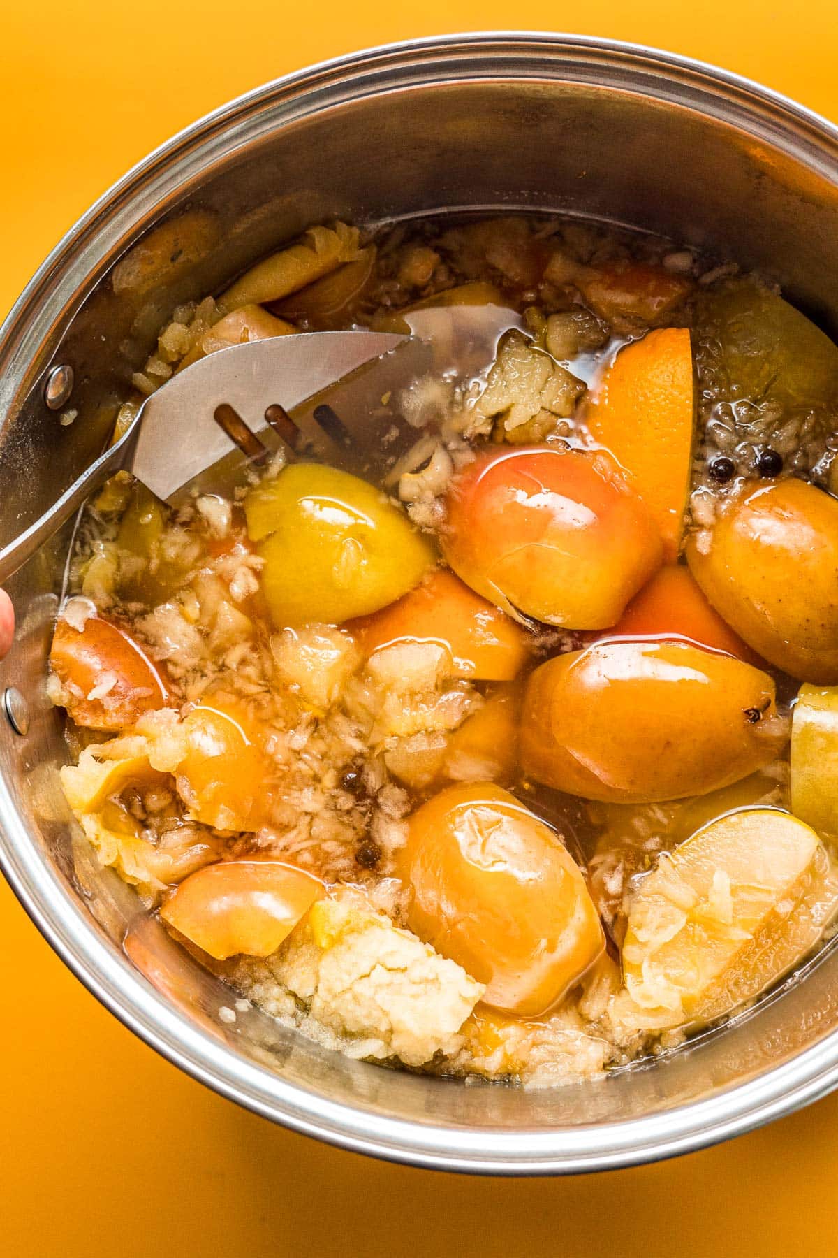 Mashing cooked apples in a stock pot.