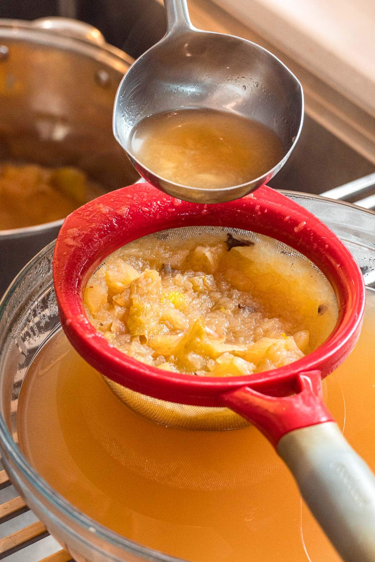 Straining apple cider from cooked apples using a fine mesh strainer.