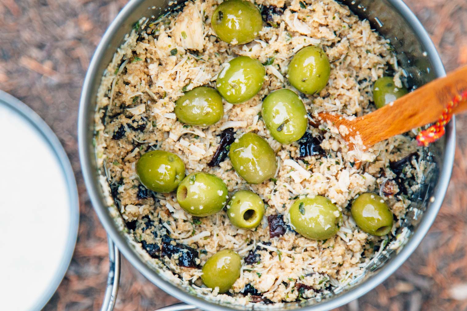 A wooden spoon in a pot that is filled with couscous and green olives