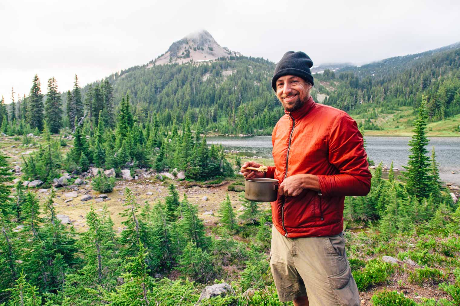 Michael is standing and holding a backpacking pot there's a mountain in the distance