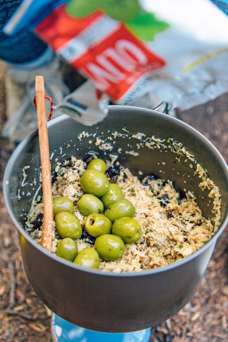 A wooden spoon in a pot that is filled with couscous and green olives