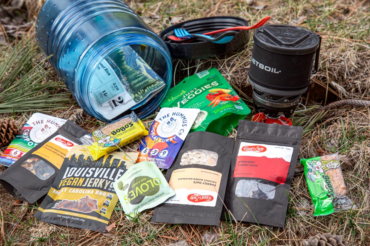 A bear canister with a spread of vegan backpacking meals