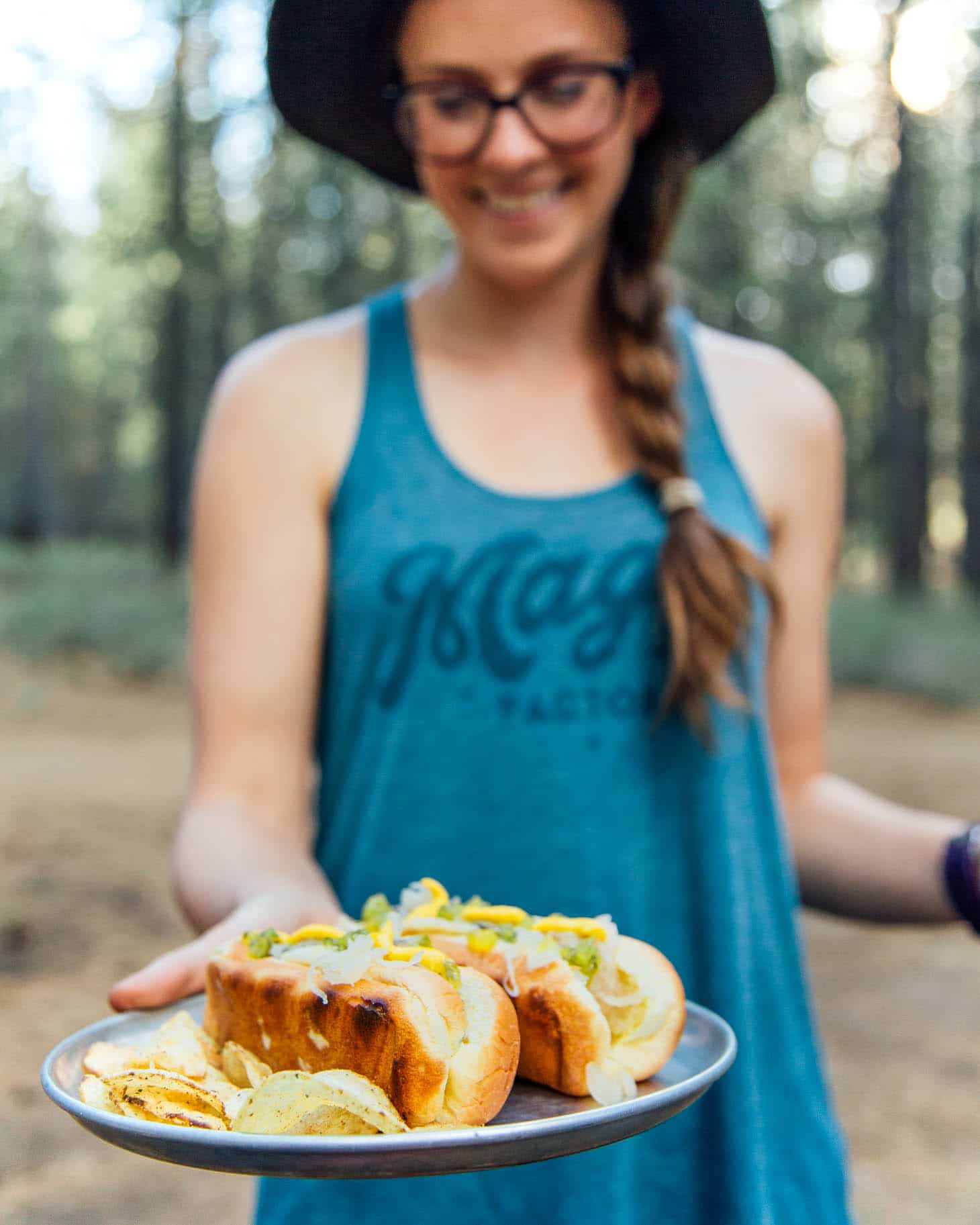 Megan holding out a plate with two hotdogs in buns and chips on the side