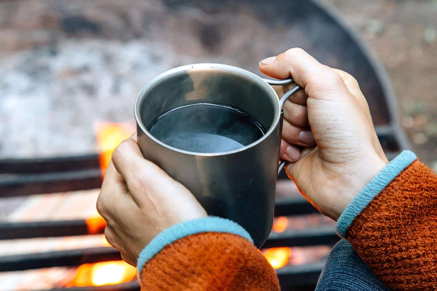 Megan holding a cup of coffee near a campfire